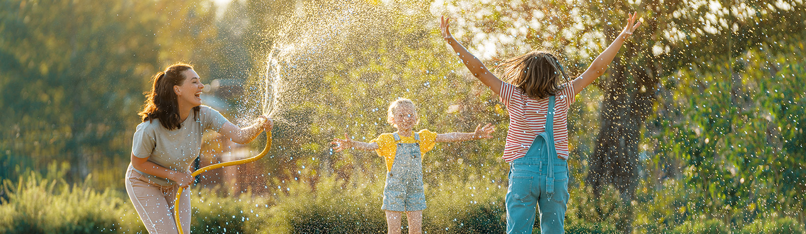 Woman holding hose, two kids outside